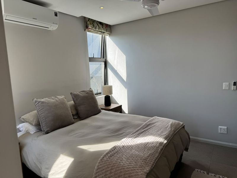 A well-maintained bedroom featuring tiled flooring, a ceiling fan, and a wall-mounted split-system air conditioner.