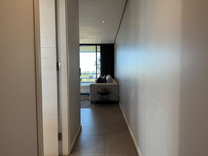 A view through a hallway leading into a living area with large sliding glass doors and tiled flooring.