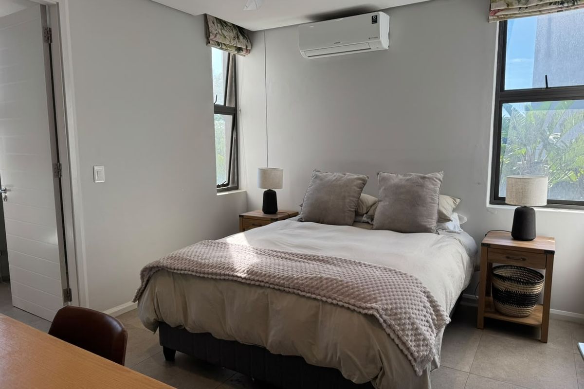 A well-maintained bedroom featuring tiled flooring, a split-system air conditioner, ceiling fan, and large windows providing natural light.