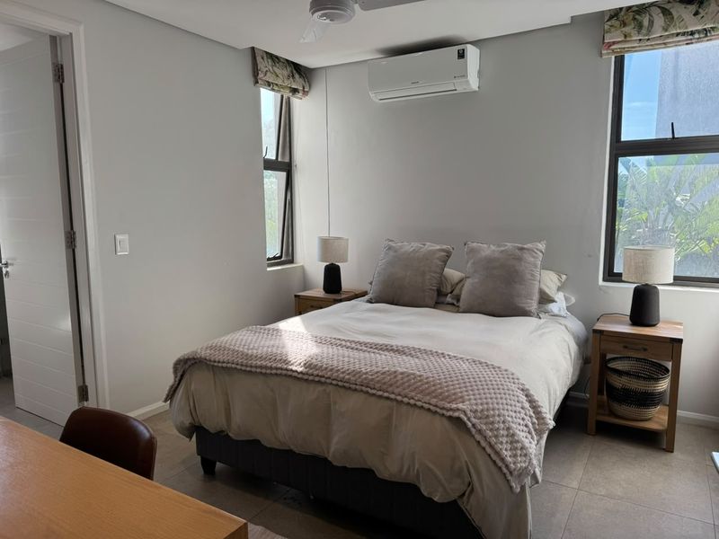 A well-maintained bedroom featuring tiled flooring, a split-system air conditioner, ceiling fan, and large windows providing natural light.