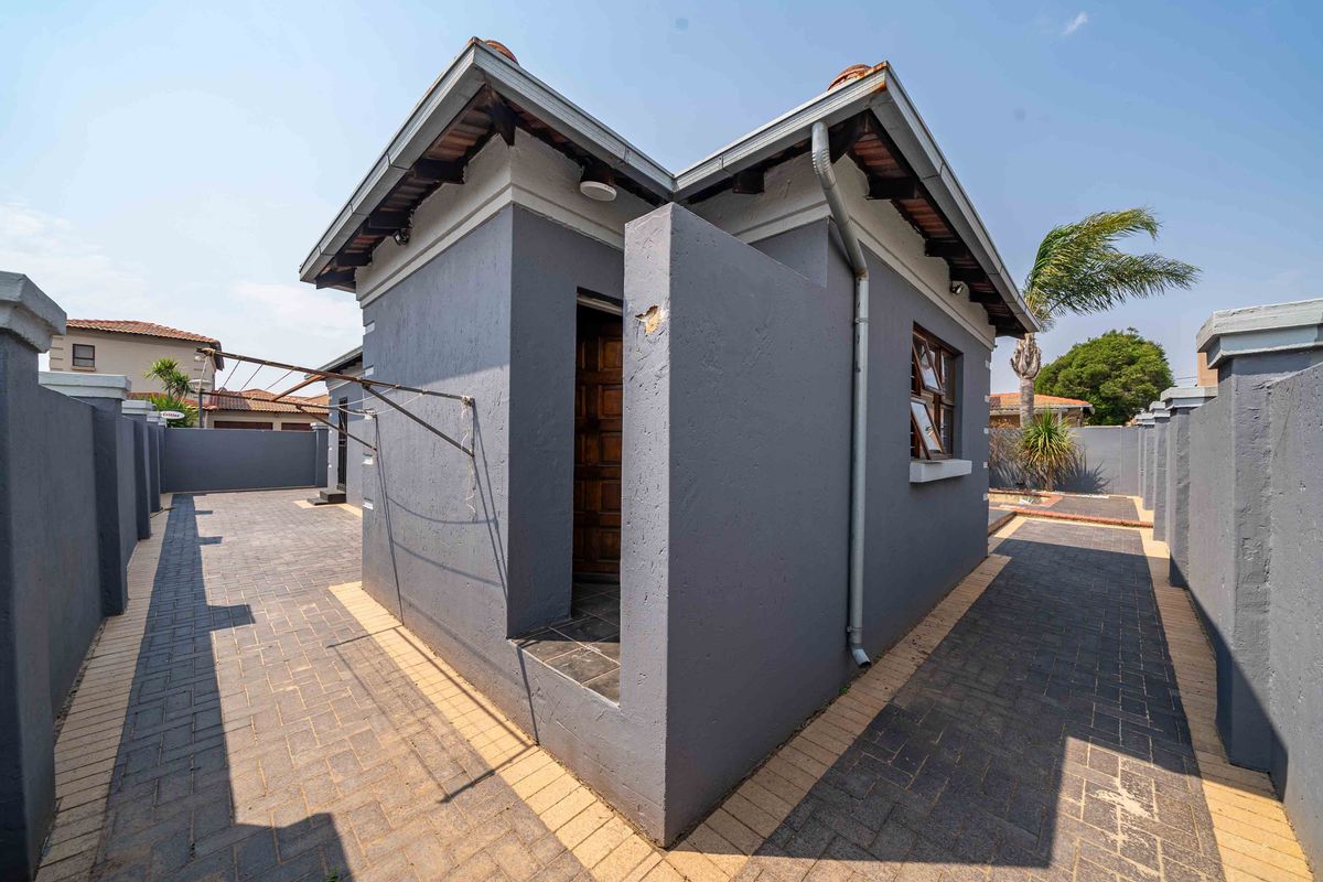 A view of the rear exterior area featuring paved courtyard space, downpipes, and a wall-mounted clothesline attached to the side of the building.