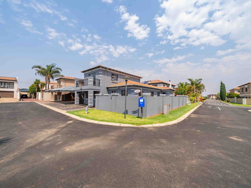 A corner-lot residential property featuring a modern grey facade, tiled roof, balcony, and paved driveway within a secure estate setting.
