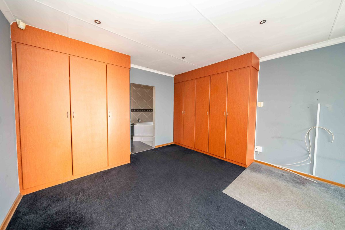 Spacious bedroom featuring extensive built-in wooden cabinetry, recessed lighting, and direct access to an en-suite bathroom area.
