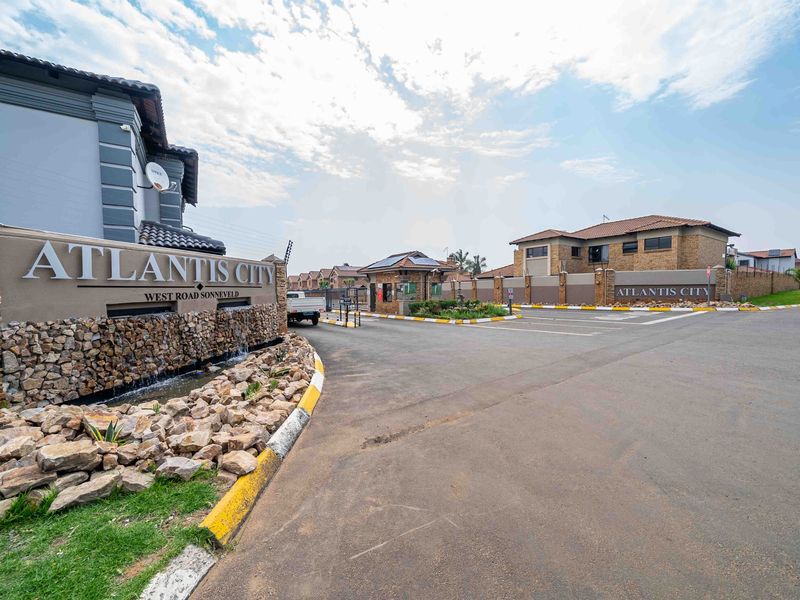 The entrance to Atlantis City estate featuring a stone-clad wall, water feature, paved driveway, and secure gated access.
