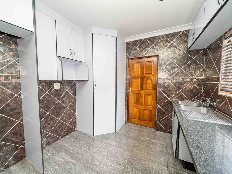 A functional kitchen featuring granite countertops, a double sink, tiled backsplash, and ample built-in cabinetry with a classic timber door.