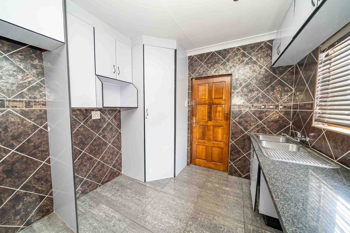 A functional kitchen featuring granite countertops, a double sink, tiled backsplash, and ample built-in cabinetry with a classic timber door.