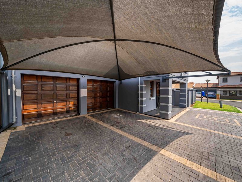 Front exterior view featuring a paved driveway, double garage with wooden doors, and a large shade sail covering the parking area.