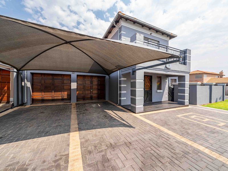 Front exterior view of a double-story house featuring a paved driveway, double garage with wooden doors, and a protective shade sail.