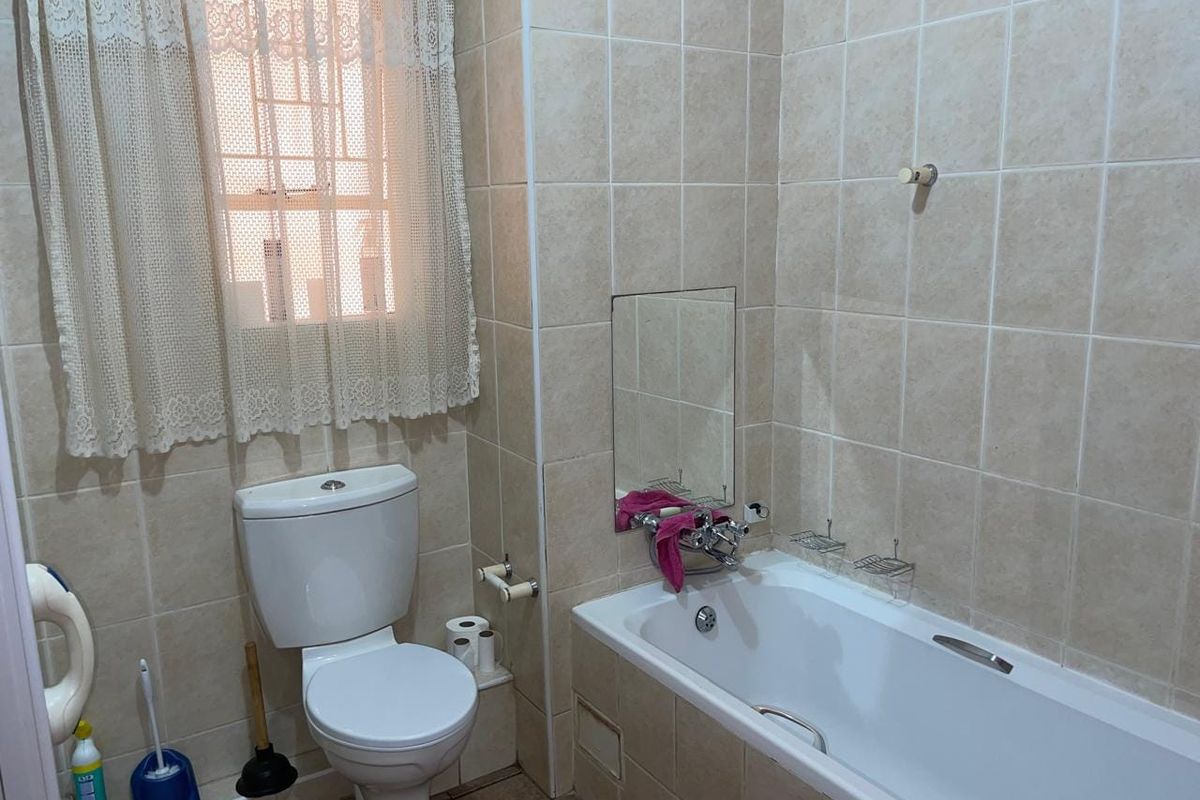 A functional bathroom featuring a bathtub, toilet, and neutral wall tiling, complete with a window for natural light and ventilation.