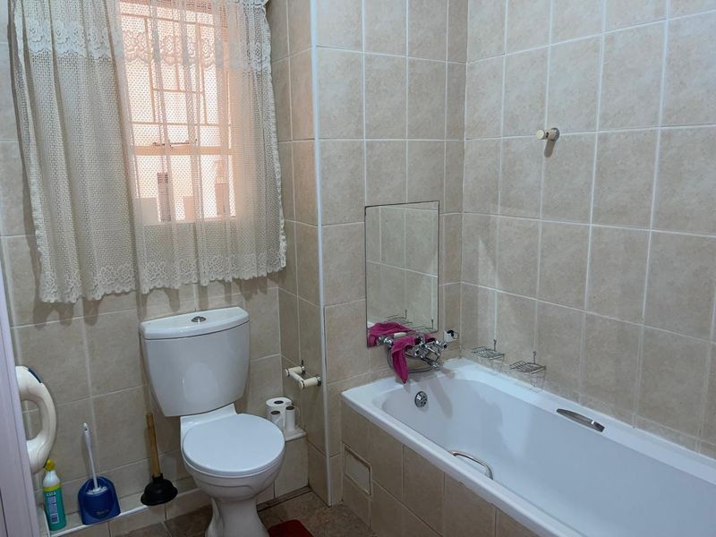 A functional bathroom featuring a bathtub, toilet, and neutral wall tiling, complete with a window for natural light and ventilation.