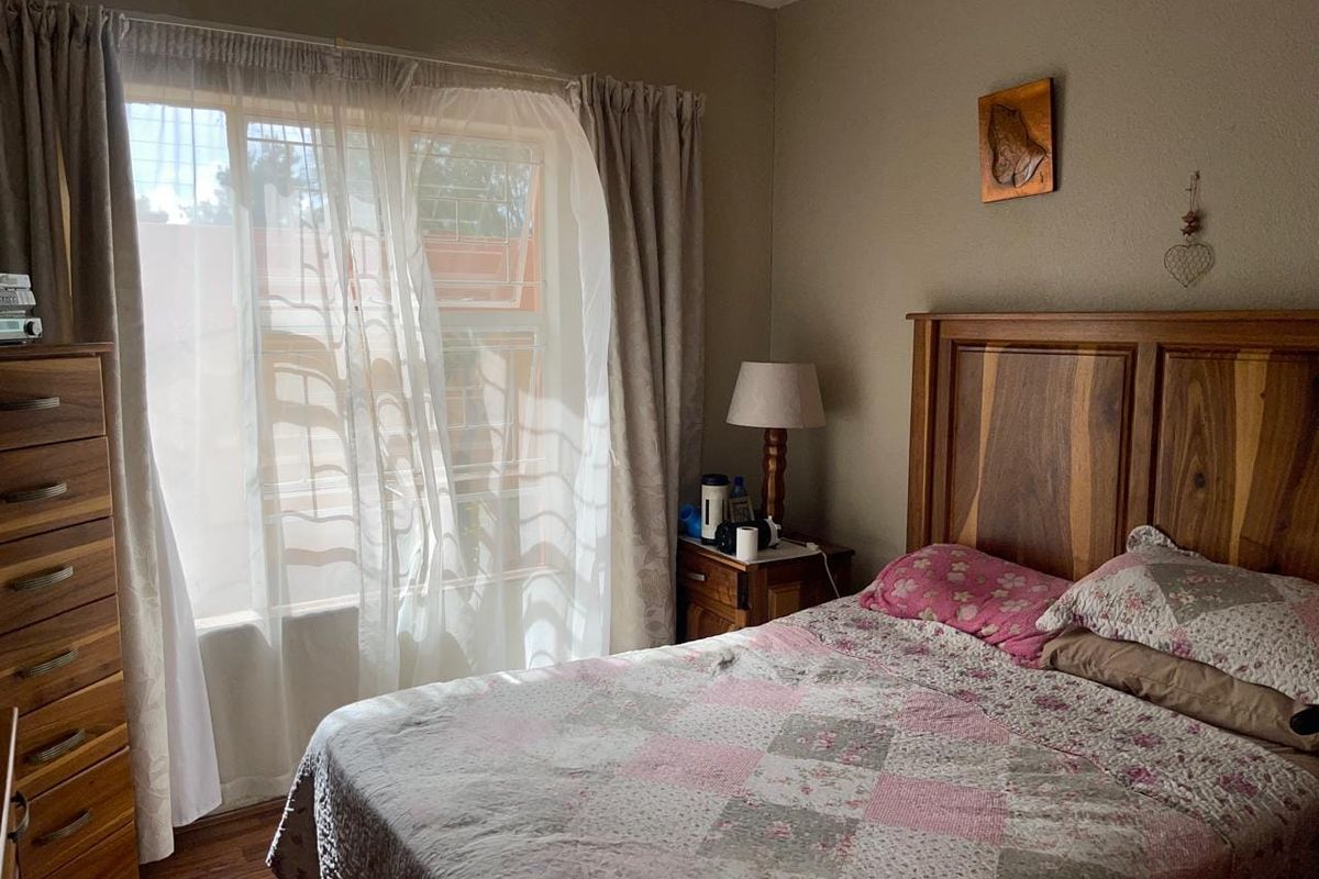 A cozy bedroom featuring laminate flooring and a window fitted with security bars, providing natural light and a functional living space.