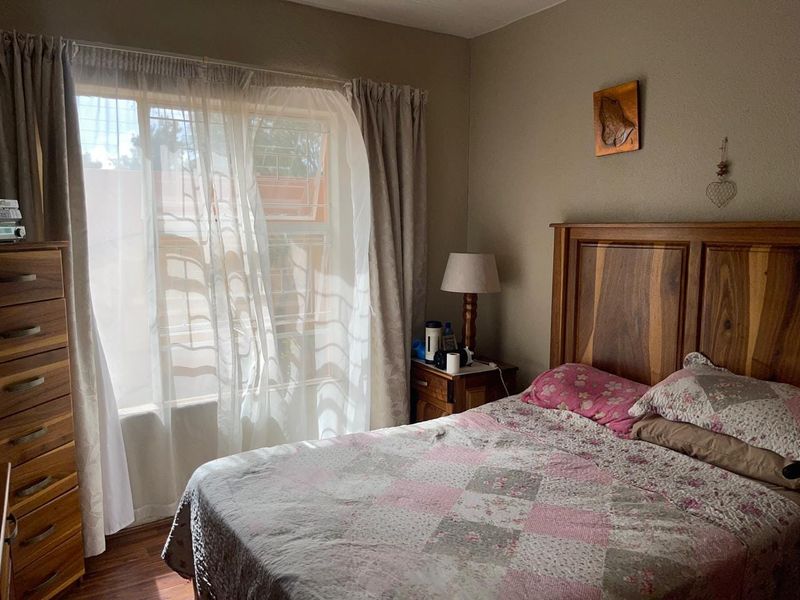 A cozy bedroom featuring laminate flooring and a window fitted with security bars, providing natural light and a functional living space.