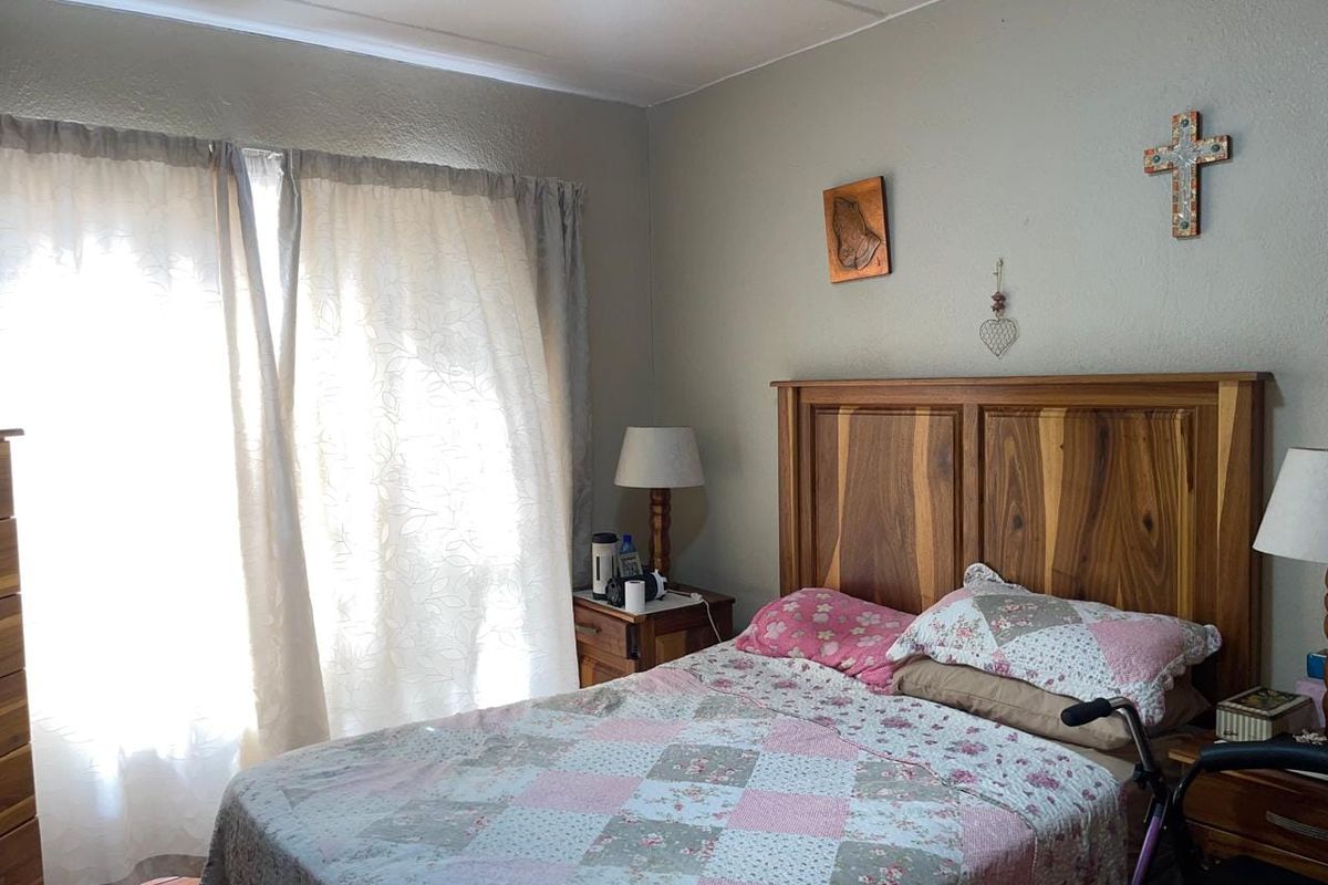 A functional bedroom featuring neutral wall finishes and natural light through large window coverings.
