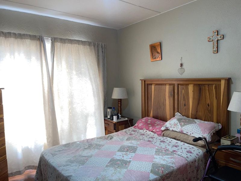 A functional bedroom featuring neutral wall finishes and natural light through large window coverings.