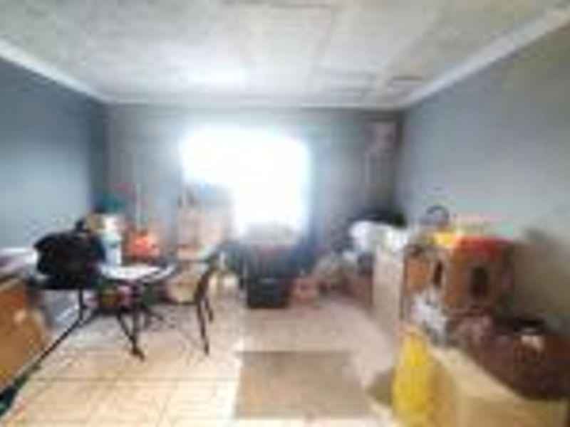 A living room space featuring tiled flooring and ceiling cornicing, currently requiring cosmetic updates to the wall finishes and ceiling surface.