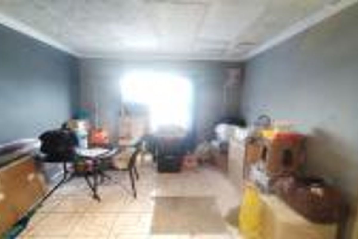 A living room space featuring tiled flooring and ceiling cornicing, currently requiring cosmetic updates to the wall finishes and ceiling surface.
