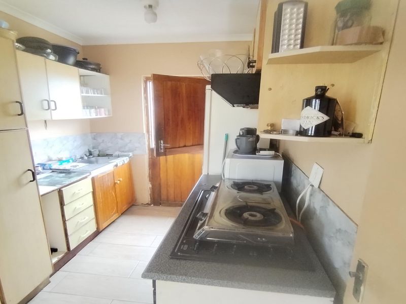 A functional kitchen featuring built-in cabinetry, a gas hob with extractor fan, and tiled flooring, offering potential for a modern renovation.
