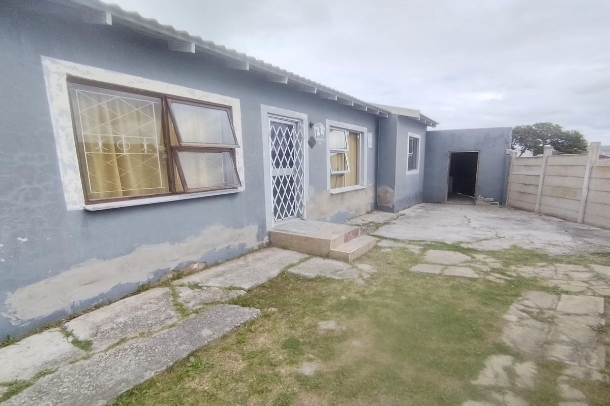 Rear exterior view of the house featuring a concrete patio area, security gate, and precast boundary walling with visible wear to the exterior facade.