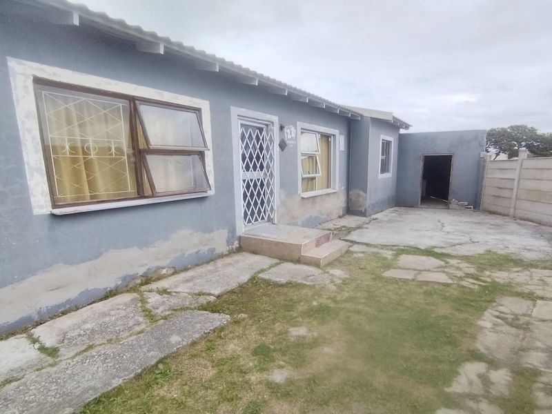 Rear exterior view of the house featuring a concrete patio area, security gate, and precast boundary walling with visible wear to the exterior facade.
