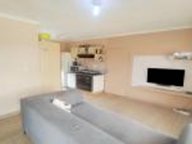 Open plan living area featuring a compact kitchen with built-in cabinetry and a dedicated media wall unit.