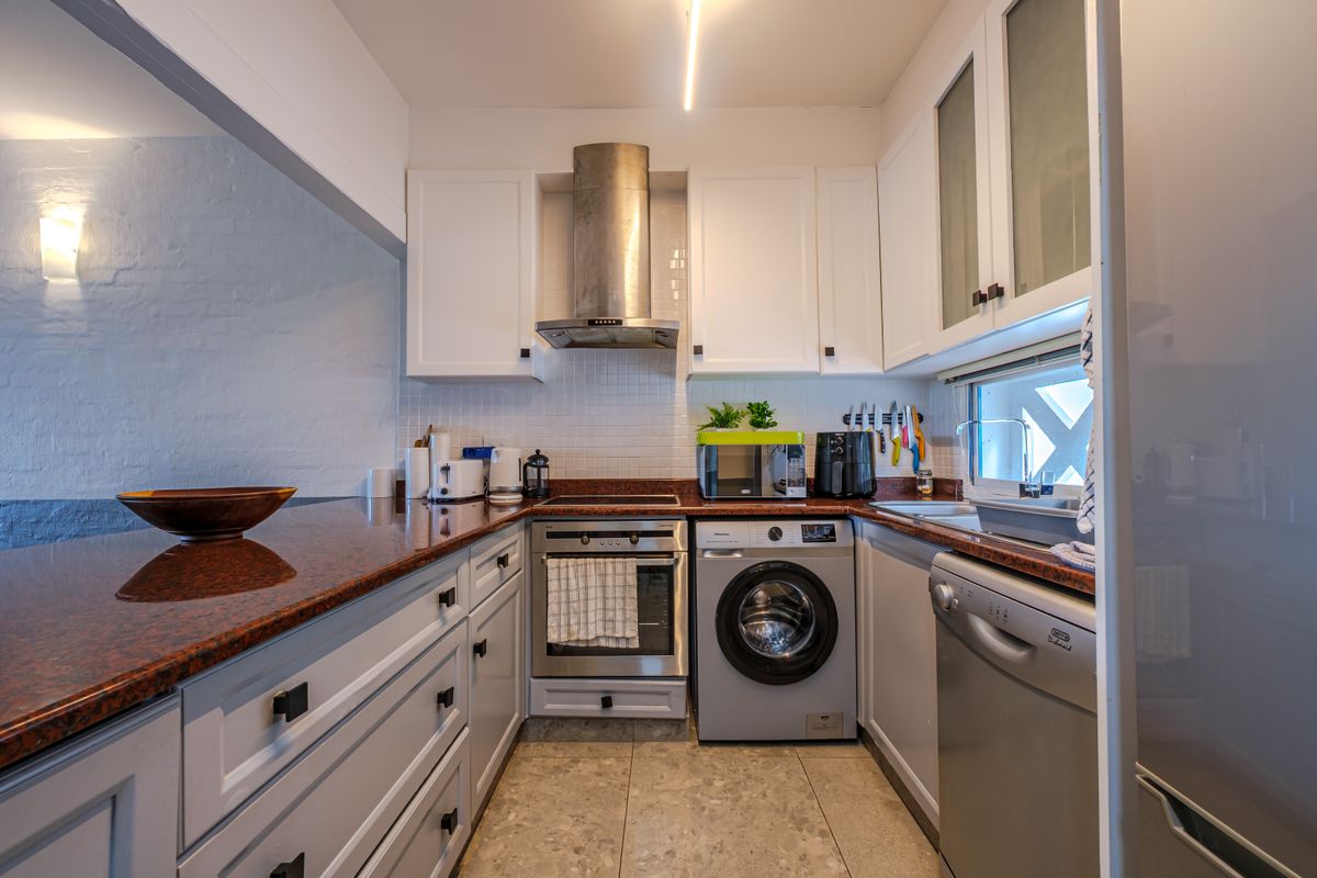 A functional kitchen featuring white cabinetry, granite countertops, a stainless steel extractor fan, built-in oven, and integrated laundry and dishwasher appliances.