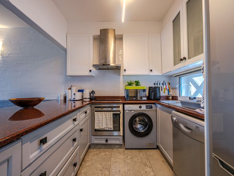 A functional kitchen featuring white cabinetry, granite countertops, a stainless steel extractor fan, built-in oven, and integrated laundry and dishwasher appliances.