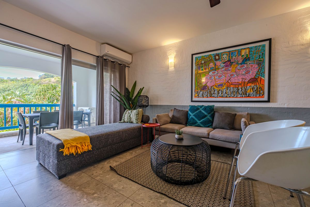 A bright living room featuring tiled floors, wall-mounted air conditioning, and large sliding doors providing seamless access to an outdoor balcony area.
