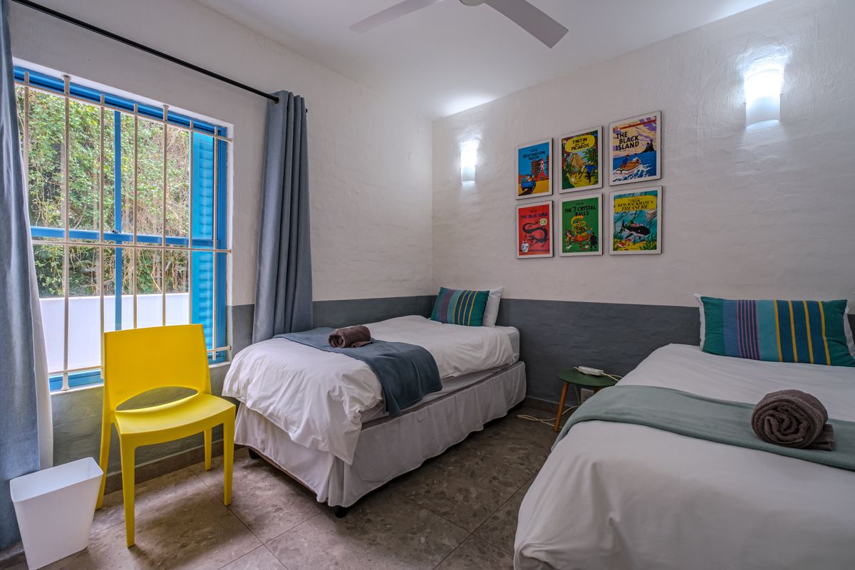 A bedroom featuring tiled flooring, wall sconces, a ceiling fan, and a window fitted with security bars.