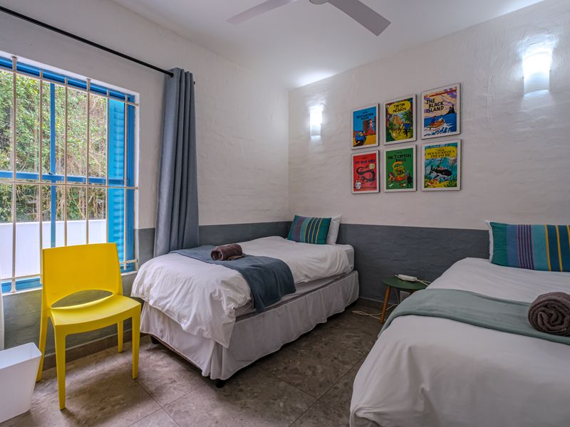 A bedroom featuring tiled flooring, wall sconces, a ceiling fan, and a window fitted with security bars.