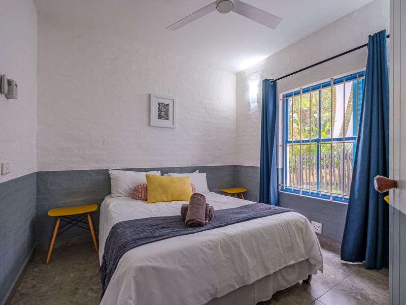 A cozy bedroom featuring textured walls, a ceiling fan, and a window with security bars, providing a functional and comfortable sleeping space.