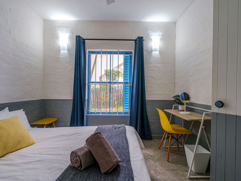 A well-lit bedroom featuring textured walls, tiled flooring, and a window fitted with security bars.