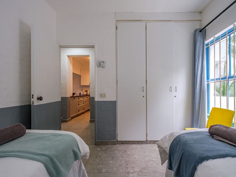 Bedroom featuring built-in cupboards, tiled flooring, and a window with security bars, with an adjacent view into the kitchen area.