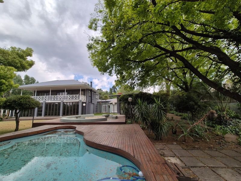 Spacious outdoor entertainment area featuring a swimming pool with timber decking, overlooking a lush garden and the rear elevation of the house.