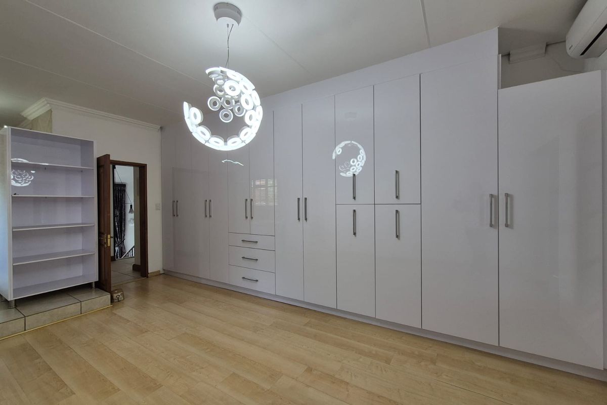 Spacious bedroom featuring extensive white built-in cupboards, light laminate flooring, and a modern pendant light fixture.