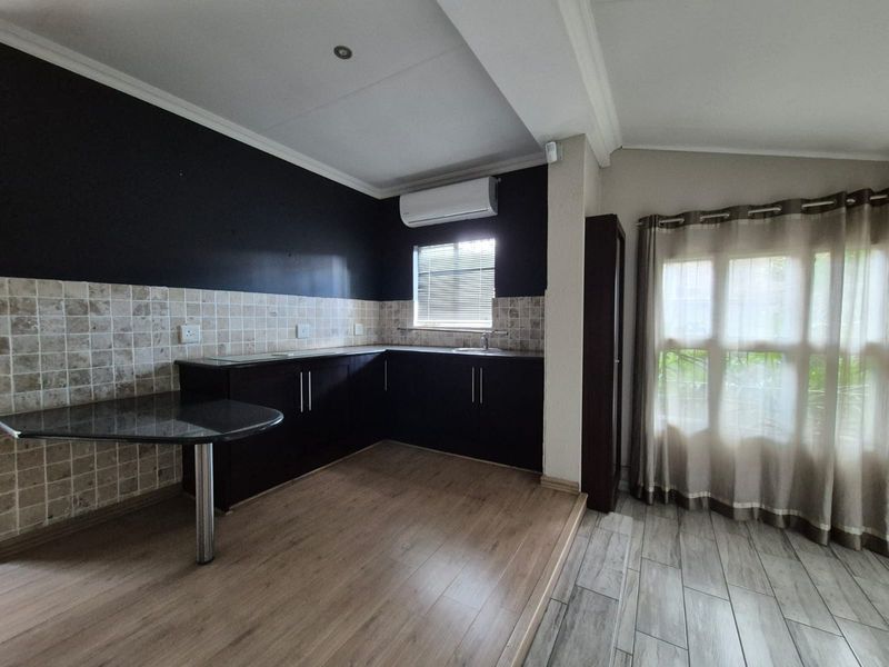 A clean, modern kitchen featuring dark cabinetry, granite countertops, a tiled backsplash, and an integrated air conditioning unit.