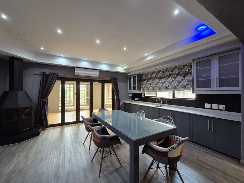 Spacious open-plan living and kitchen area featuring modern grey cabinetry, a freestanding fireplace, recessed lighting, and seamless access to the outdoor patio.