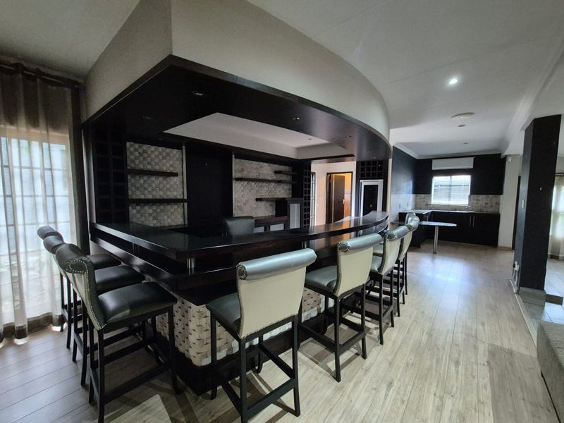 A well-appointed built-in bar area featuring a curved counter, integrated shelving, and modern finishes, seamlessly connected to the adjacent kitchen space.