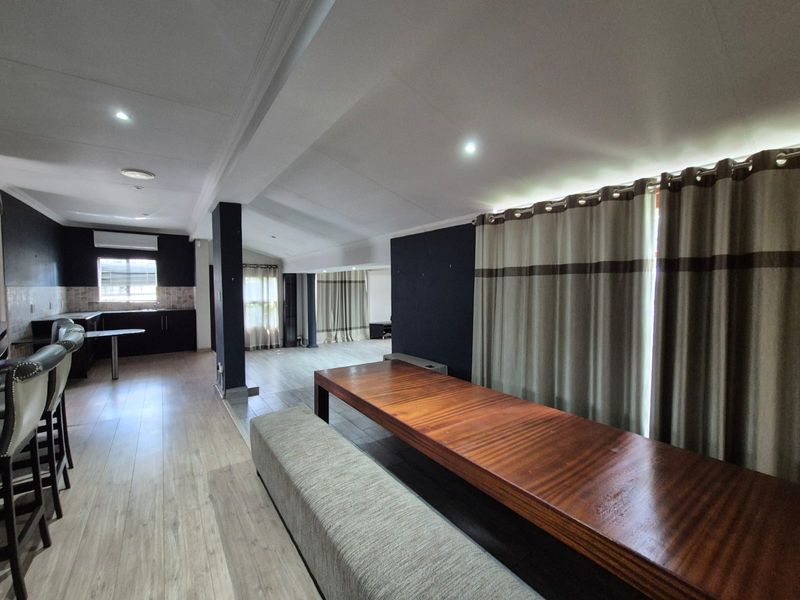 Spacious open-plan living and kitchen area featuring modern laminate flooring, recessed lighting, and a functional kitchen layout with dark cabinetry.