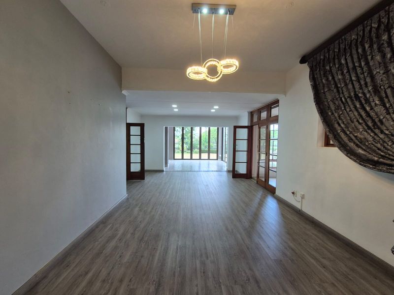 Spacious, light-filled living area featuring modern laminate flooring, recessed lighting, and large timber-framed glass doors leading to the outdoor space.