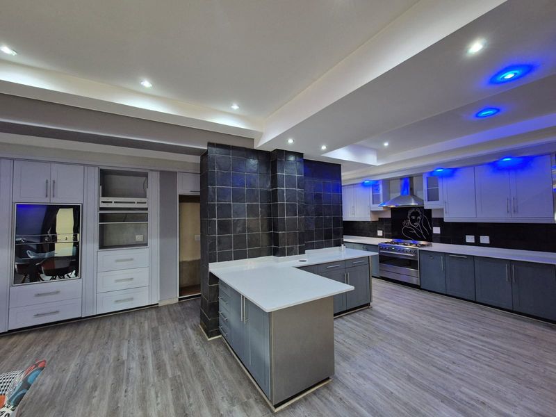 Modern kitchen featuring a central island, stone countertops, built-in oven, gas stove with extractor, and contemporary cabinetry with integrated lighting.