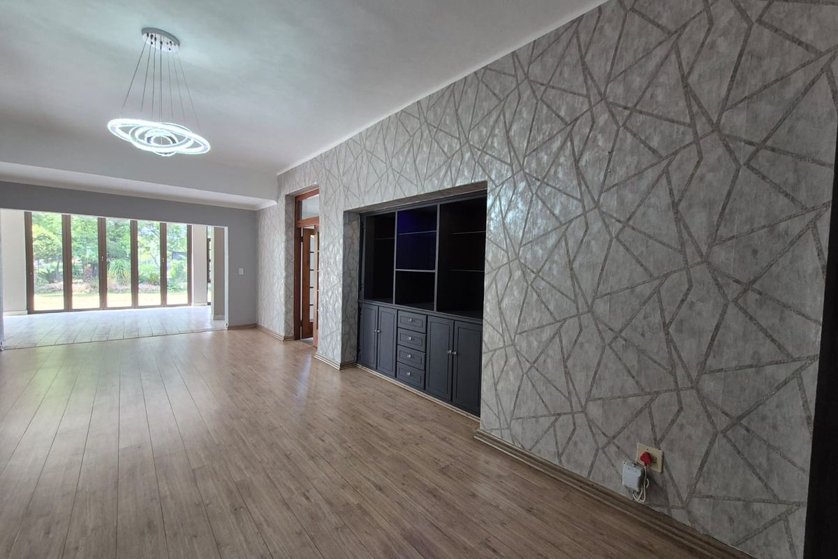 Spacious living area featuring laminate flooring, modern feature wallpaper, built-in cabinetry, and large sliding glass doors leading to an outdoor space.