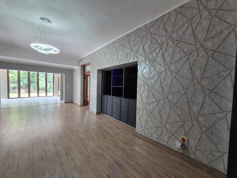 Spacious living area featuring laminate flooring, modern feature wallpaper, built-in cabinetry, and large sliding glass doors leading to an outdoor space.