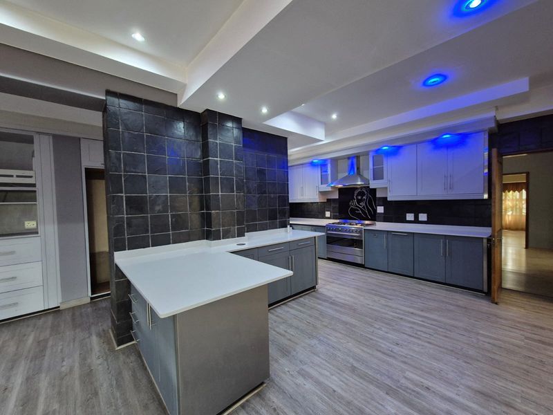 Modern kitchen featuring sleek grey cabinetry, stone countertops, stainless steel appliances, and striking tiled feature walls with integrated ambient lighting.