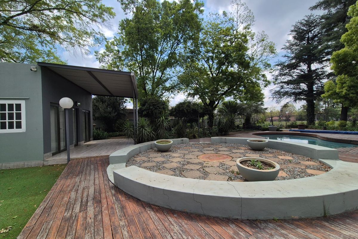 Rear garden area featuring a swimming pool, covered patio, and a circular concrete planter set within weathered wooden decking.