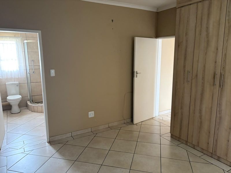 A vacant bedroom featuring tiled flooring, built-in wooden cupboards, and an en-suite bathroom access point.