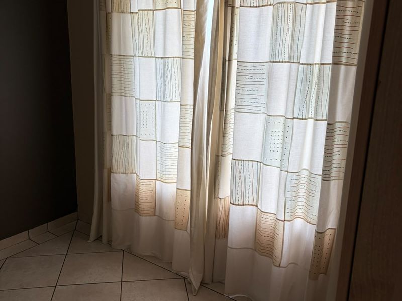 A simple bedroom space featuring neutral ceramic floor tiles and window curtains, offering a blank canvas for interior design.