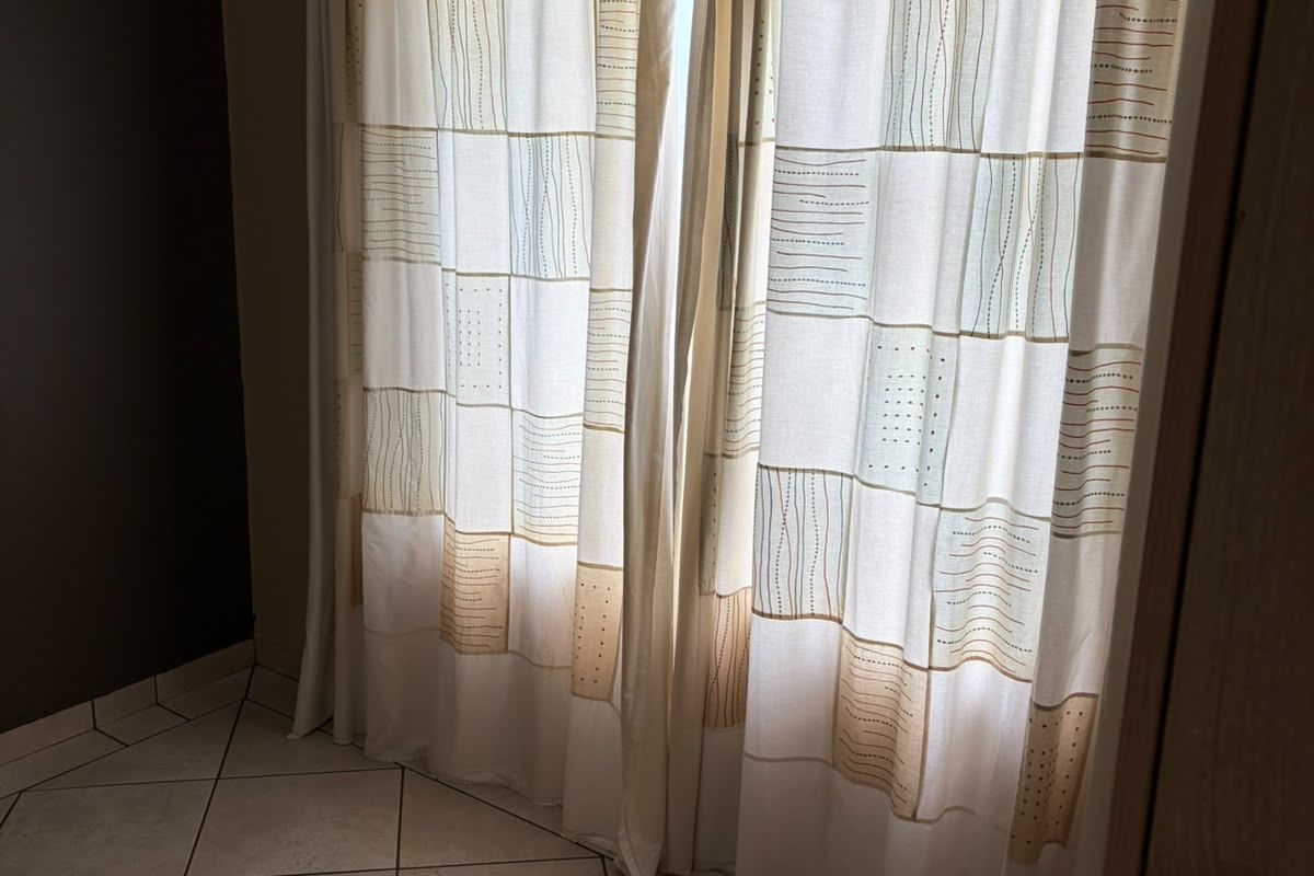 A simple bedroom space featuring neutral ceramic floor tiles and window curtains, offering a blank canvas for interior design.