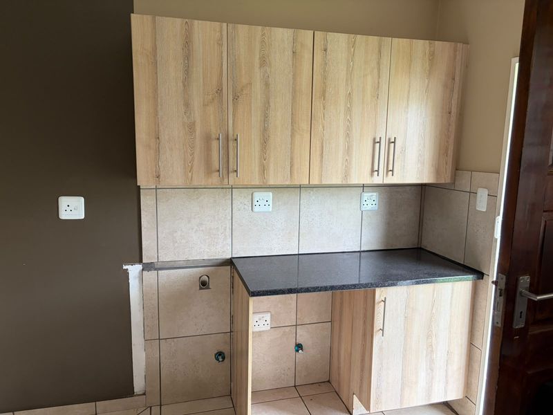A functional scullery or utility area featuring light wood-finish cabinetry, dark laminate countertops, and tiled backsplash with dedicated plumbing and electrical points.