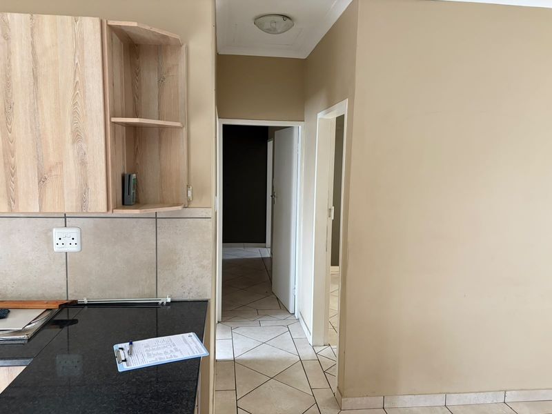 A functional kitchen area featuring laminate cabinetry, granite countertops, and tiled flooring, leading into a hallway with access to other rooms.
