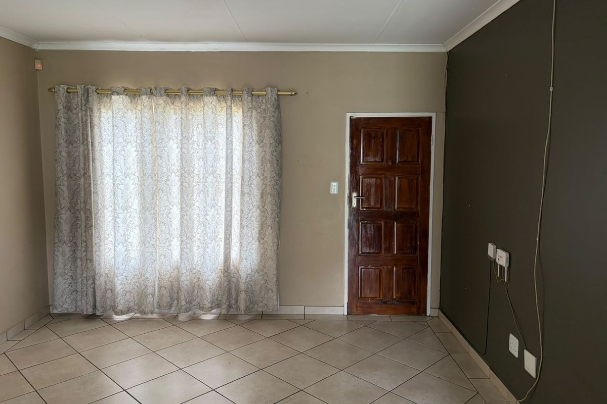 An empty living room featuring tiled flooring, a wooden entrance door, and neutral wall tones, providing a blank canvas for personalization.